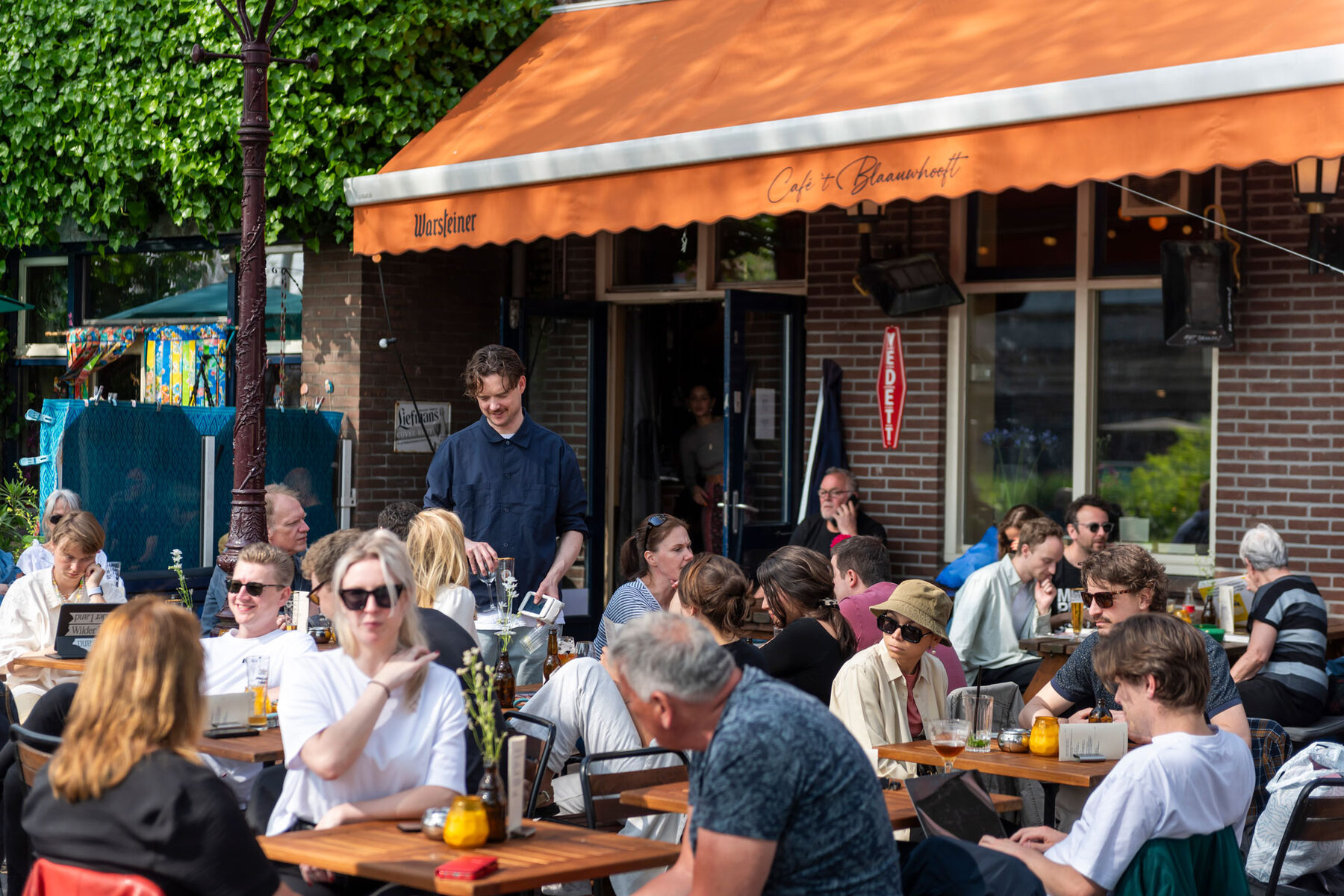 Druk zonnig terras onder de oranje luifel